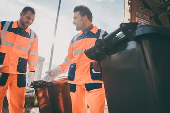 Two garbage men dressed in bright colored uniforms working with two garbage cans at Addison Ranch Apartments, California